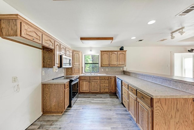 kitchen featuring kitchen peninsula, appliances with stainless steel finishes, backsplash, and light hardwood / wood-style flooring