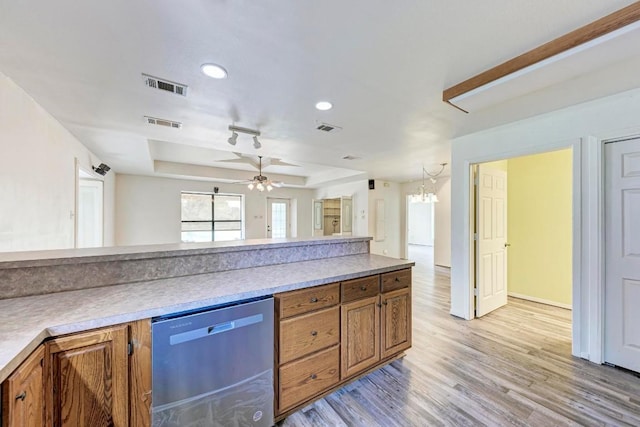 kitchen featuring a raised ceiling, stainless steel dishwasher, ceiling fan with notable chandelier, and light wood-type flooring