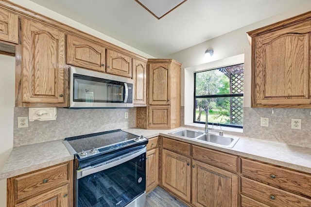 kitchen with appliances with stainless steel finishes, backsplash, light hardwood / wood-style flooring, and sink