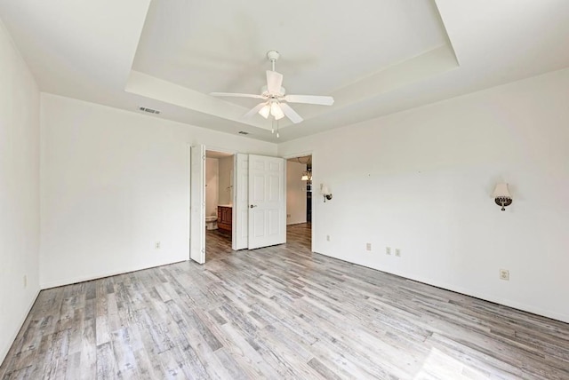 unfurnished bedroom featuring light hardwood / wood-style floors, a raised ceiling, and ceiling fan