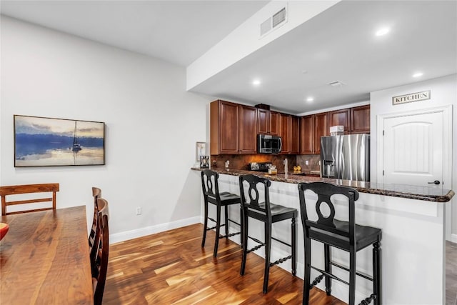 kitchen featuring kitchen peninsula, dark stone counters, stainless steel appliances, hardwood / wood-style flooring, and a breakfast bar area