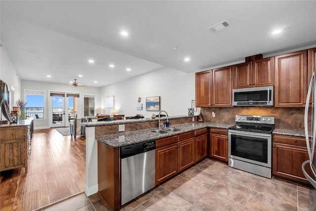 kitchen featuring kitchen peninsula, appliances with stainless steel finishes, french doors, dark stone countertops, and light hardwood / wood-style floors