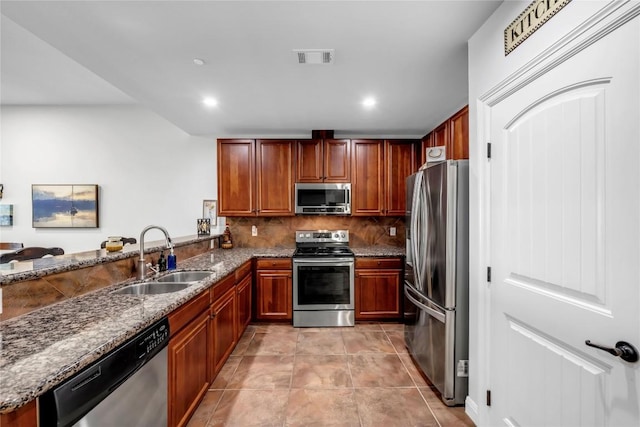 kitchen featuring kitchen peninsula, appliances with stainless steel finishes, tasteful backsplash, dark stone counters, and sink