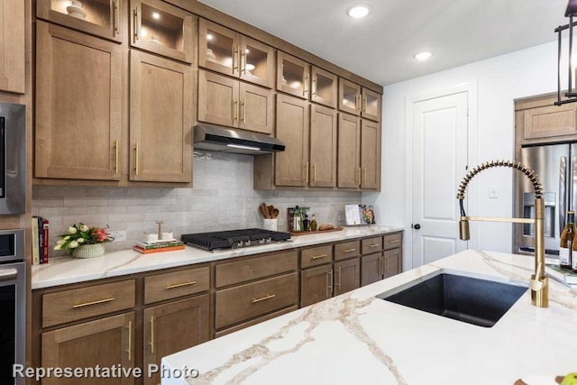 kitchen with light stone countertops, sink, tasteful backsplash, decorative light fixtures, and appliances with stainless steel finishes