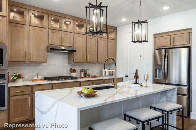 kitchen with a kitchen island with sink, an inviting chandelier, dark hardwood / wood-style floors, decorative backsplash, and appliances with stainless steel finishes