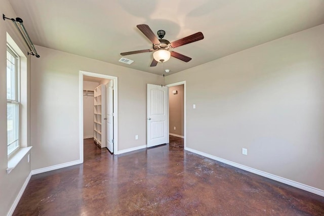 unfurnished bedroom featuring a walk in closet, ceiling fan, a closet, and multiple windows