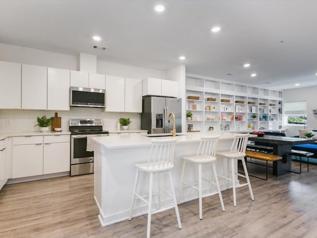 kitchen with white cabinetry, stainless steel appliances, light hardwood / wood-style floors, and a center island with sink