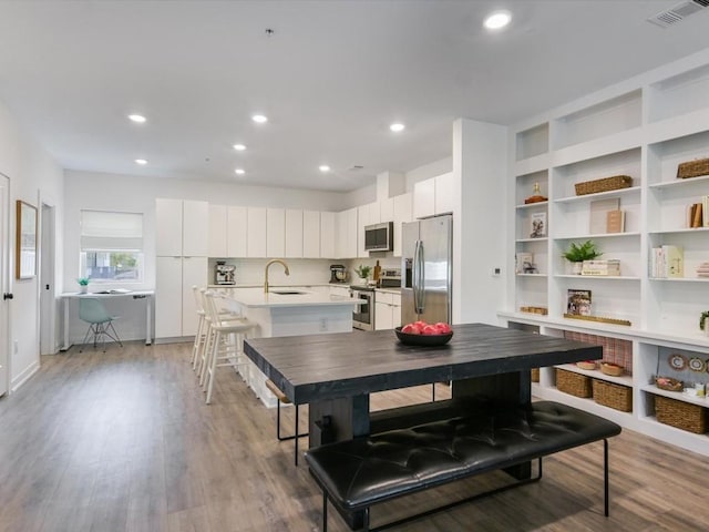 kitchen featuring sink, white cabinets, a kitchen breakfast bar, stainless steel appliances, and light wood-type flooring