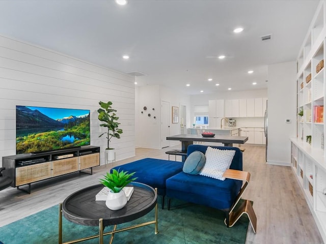 living room featuring sink, light hardwood / wood-style floors, and wood walls