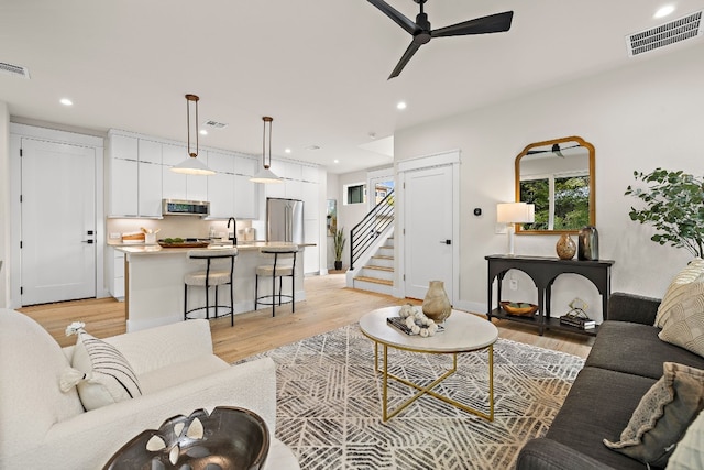 living room with ceiling fan, sink, and light wood-type flooring