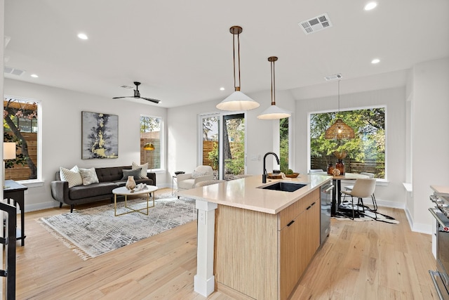 kitchen featuring ceiling fan, light brown cabinets, light wood-type flooring, and a kitchen island with sink