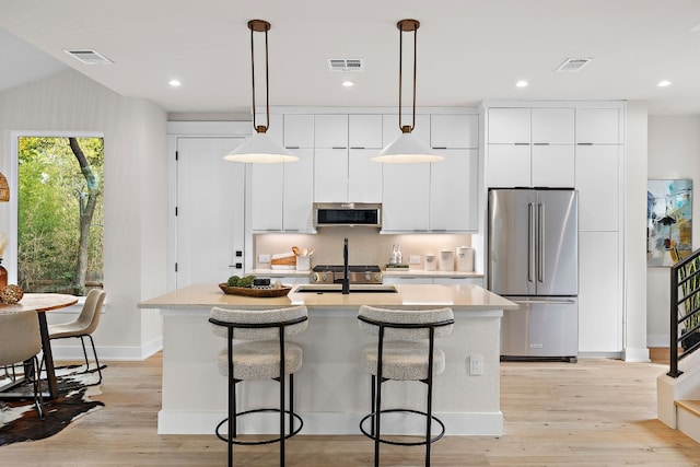 kitchen featuring hanging light fixtures, stainless steel appliances, lofted ceiling, a kitchen island with sink, and white cabinets