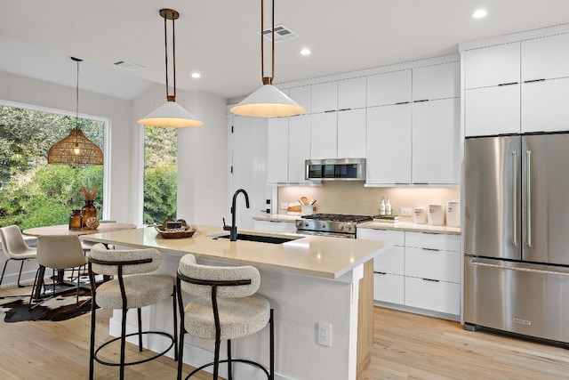 kitchen with a center island with sink, sink, decorative light fixtures, light hardwood / wood-style floors, and stainless steel appliances