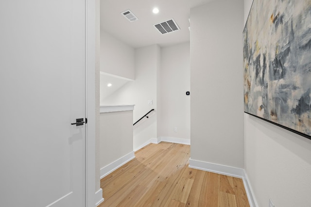 hallway with light wood finished floors, baseboards, visible vents, and an upstairs landing