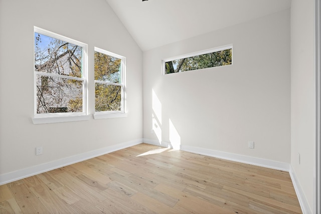 spare room with lofted ceiling, light wood-type flooring, and baseboards