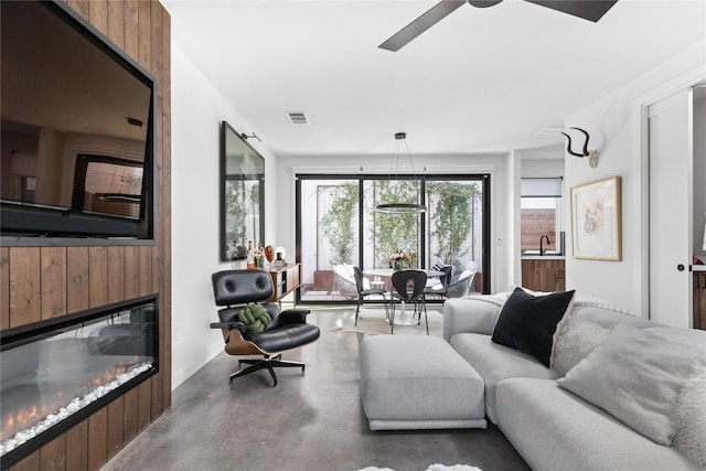 living room featuring ceiling fan, a large fireplace, concrete flooring, and sink