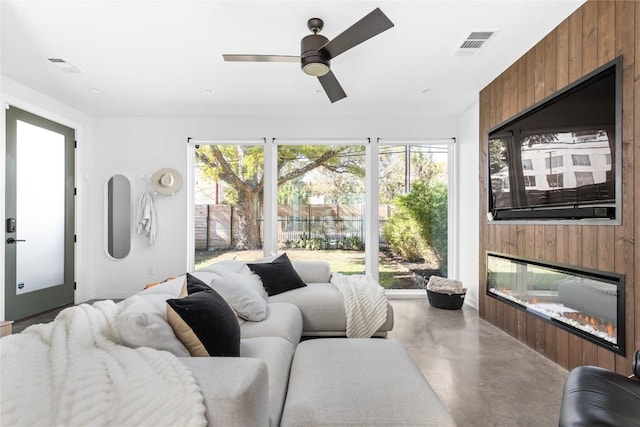 living room with a healthy amount of sunlight, wooden walls, a large fireplace, and concrete flooring