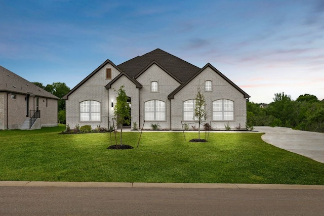 french country style house featuring brick siding and a yard