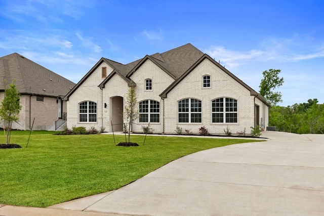 french country inspired facade with brick siding, an attached garage, driveway, and a front lawn