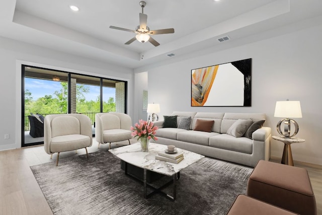 living room with light wood-style flooring, a tray ceiling, visible vents, and recessed lighting