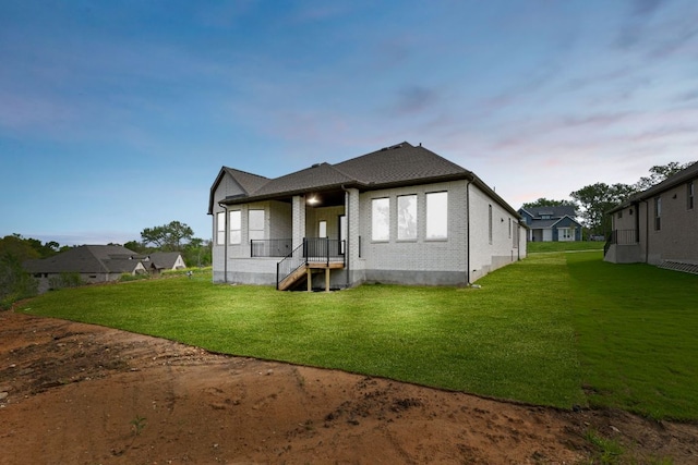 back of property at dusk with a lawn and brick siding