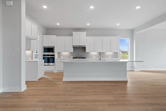 kitchen featuring oven, built in microwave, white cabinetry, decorative backsplash, and light countertops