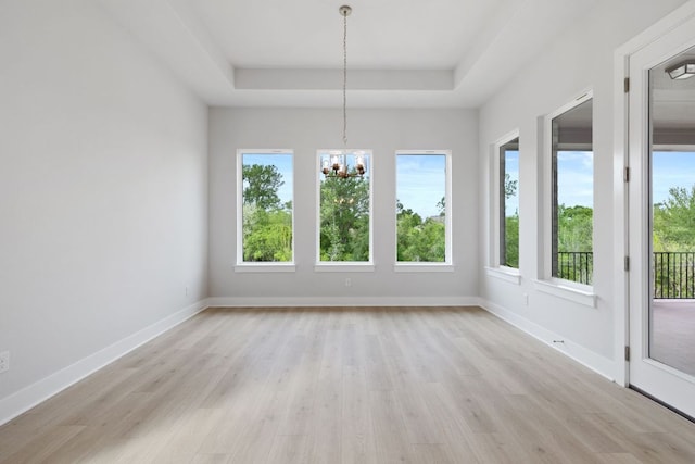 unfurnished dining area featuring light wood finished floors, a wealth of natural light, a notable chandelier, and a raised ceiling