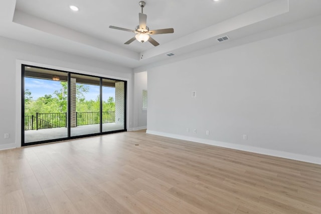 spare room featuring a raised ceiling, light wood-style flooring, visible vents, and baseboards