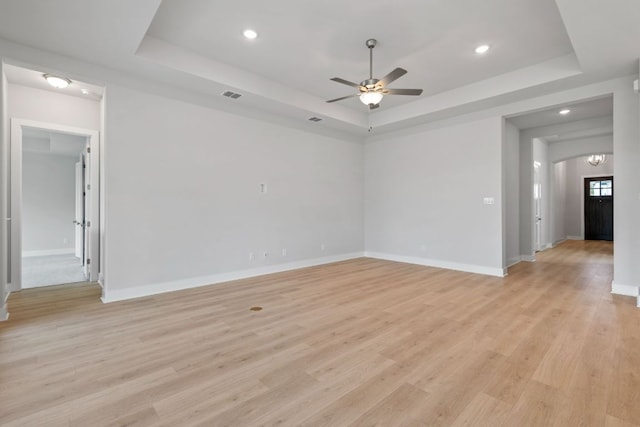 spare room featuring light wood finished floors, a tray ceiling, visible vents, a ceiling fan, and baseboards