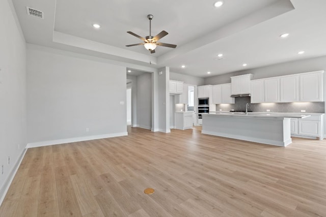 unfurnished living room featuring a ceiling fan, light wood finished floors, a tray ceiling, and visible vents