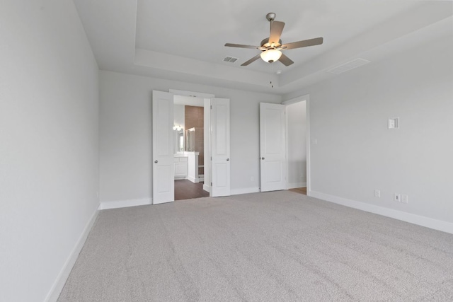 unfurnished bedroom with a tray ceiling, carpet floors, visible vents, and baseboards