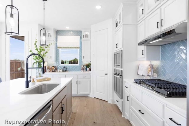 kitchen featuring sink, hanging light fixtures, stainless steel appliances, light hardwood / wood-style floors, and white cabinets