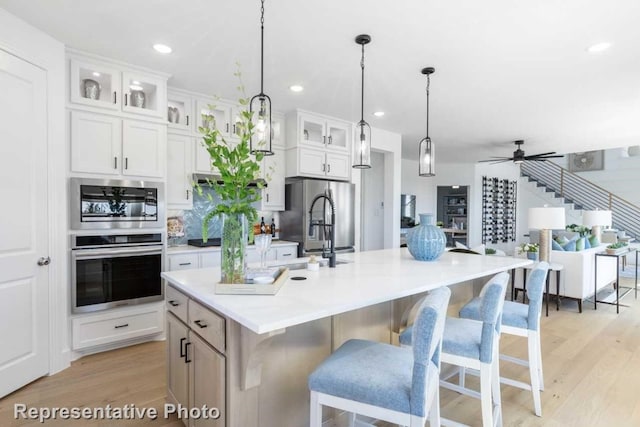 kitchen with white cabinets, a spacious island, ceiling fan, light hardwood / wood-style floors, and stainless steel appliances