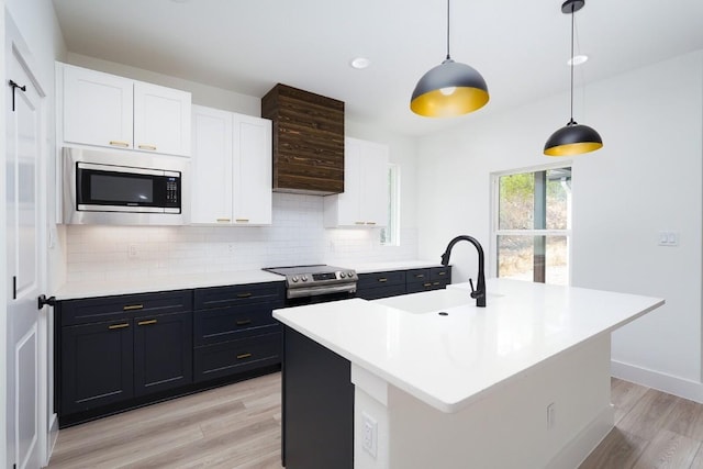 kitchen featuring a center island with sink, stainless steel appliances, decorative light fixtures, and light hardwood / wood-style flooring