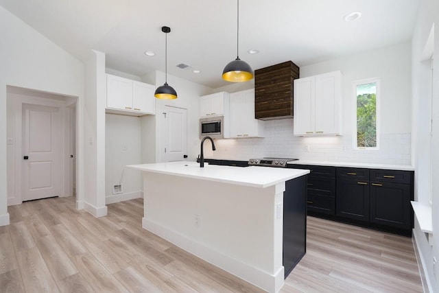 kitchen with hanging light fixtures, an island with sink, appliances with stainless steel finishes, and light hardwood / wood-style flooring