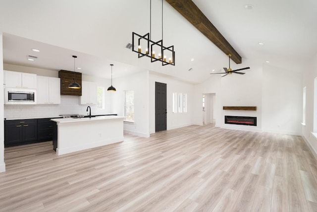 unfurnished living room with beam ceiling, ceiling fan, sink, and light wood-type flooring