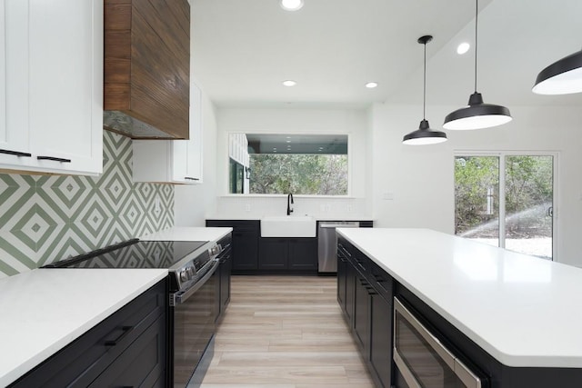 kitchen featuring appliances with stainless steel finishes, sink, light hardwood / wood-style flooring, white cabinets, and hanging light fixtures