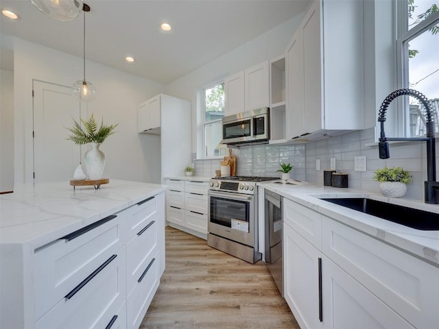 kitchen with sink, white cabinetry, stainless steel appliances, and hanging light fixtures