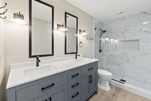 bathroom with hardwood / wood-style flooring, vanity, toilet, and a tile shower