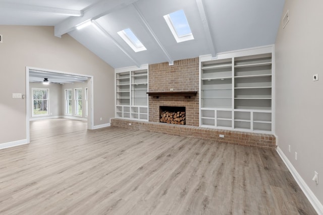 unfurnished living room featuring a brick fireplace, light hardwood / wood-style floors, lofted ceiling with skylight, and ceiling fan