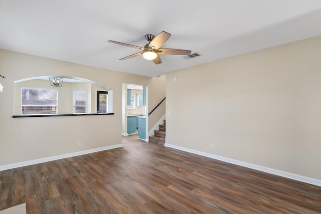 unfurnished living room featuring ceiling fan with notable chandelier and dark wood-type flooring