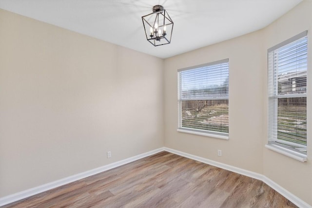 empty room featuring light hardwood / wood-style flooring, a wealth of natural light, and a notable chandelier