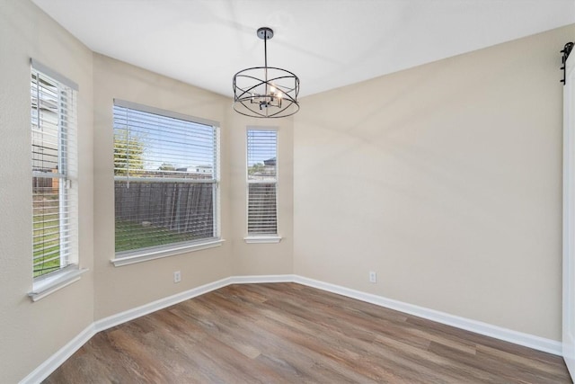 empty room with a barn door, a wealth of natural light, an inviting chandelier, and hardwood / wood-style flooring