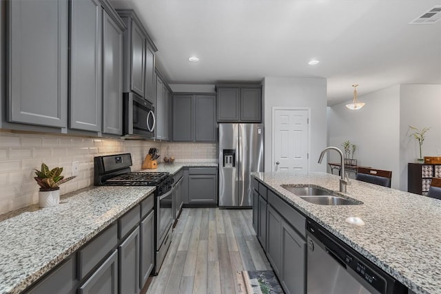 kitchen featuring appliances with stainless steel finishes, tasteful backsplash, gray cabinetry, sink, and decorative light fixtures