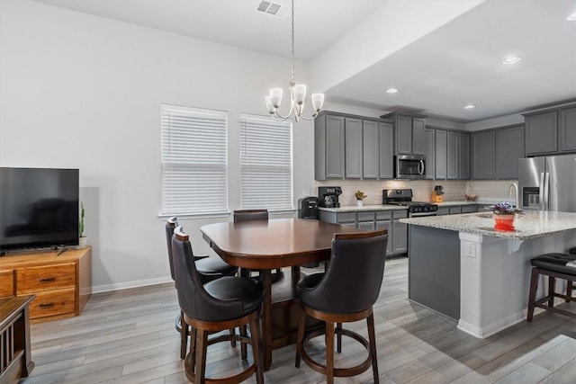 kitchen with light stone countertops, stainless steel appliances, a chandelier, gray cabinets, and a kitchen island with sink