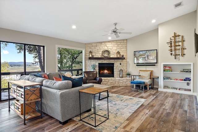 living room with vaulted ceiling, ceiling fan, hardwood / wood-style floors, and a stone fireplace