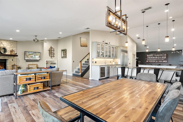 dining room with ceiling fan with notable chandelier, a fireplace, wine cooler, sink, and light wood-type flooring