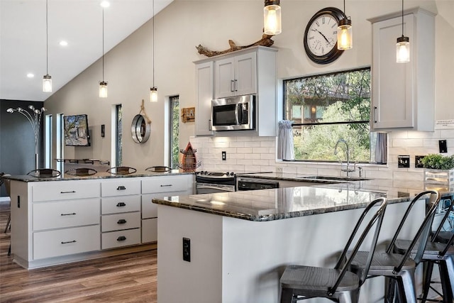 106 Center Cove Ii Loop, Spicewood, TX 78669 - kitchen with appliances with stainless steel finishes, dark stone countertops, a peninsula, a sink, and a breakfast bar