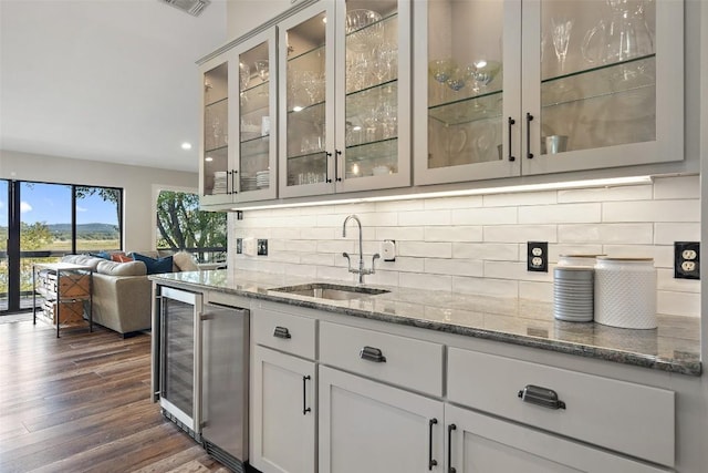 bar with dark hardwood / wood-style flooring, decorative backsplash, light stone counters, and sink