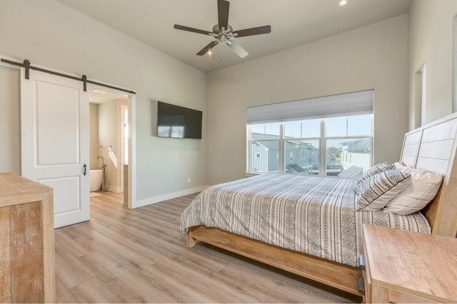 bedroom with a barn door, light hardwood / wood-style floors, ceiling fan, and connected bathroom